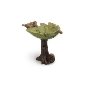 May include: A small bird bath made of resin, shaped like a leaf on a tree trunk. The bird bath is green and brown with two small birds perched on the edge.