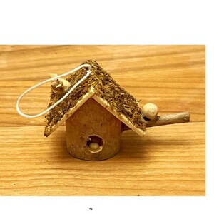 May include: A small wooden birdhouse with a moss roof and a white string attached to the top. The birdhouse has a small hole for birds to enter and a small wooden perch on the side.