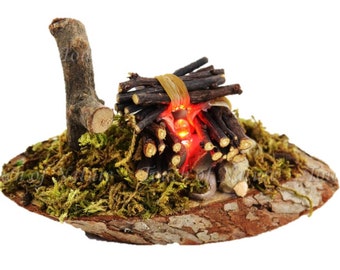 Könnte beinhalten: Eine Miniatur-Lagerfeuerszene mit einem Haufen Reisig, einem kleinen Ast und roten LED-Lichtern, die Flammen simulieren. Die Szene ist auf einem runden Sockel aus Rinde und Moos aufgebaut.