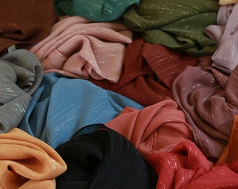 May include: A pile of colorful scarves with a shimmery metallic finish. The scarves are made of a soft, flowing fabric and are available in a variety of colors, including pink, blue, green, red, and orange.