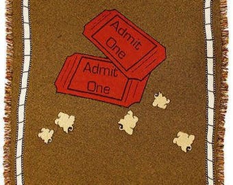 May include: A brown woven throw blanket with a red and white "Admit One" ticket design and white popcorn scattered on the blanket.