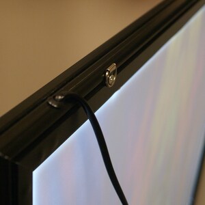 May include: A black framed light box with a white light panel and a black cord hanging from the top. The frame has a silver metal latch.