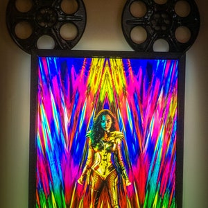 May include: A framed movie poster for the film Wonder Woman 1984. The poster features a colorful abstract background with Wonder Woman in the center, wearing her golden armor. The text "JUNE 5, 2020" is at the bottom of the poster.