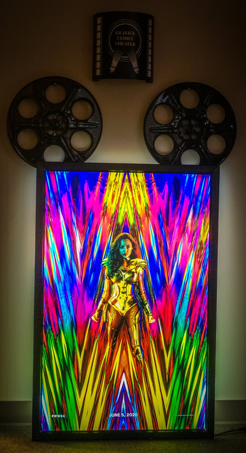 May include: A framed movie poster for the film Wonder Woman 1984. The poster features a colorful abstract background with Wonder Woman in the center, wearing her golden armor. The text "JUNE 5, 2020" is at the bottom of the poster.