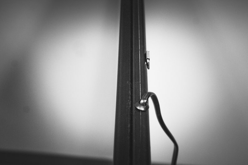May include: A black metal rod with a silver metal hook and a black strap attached to it.