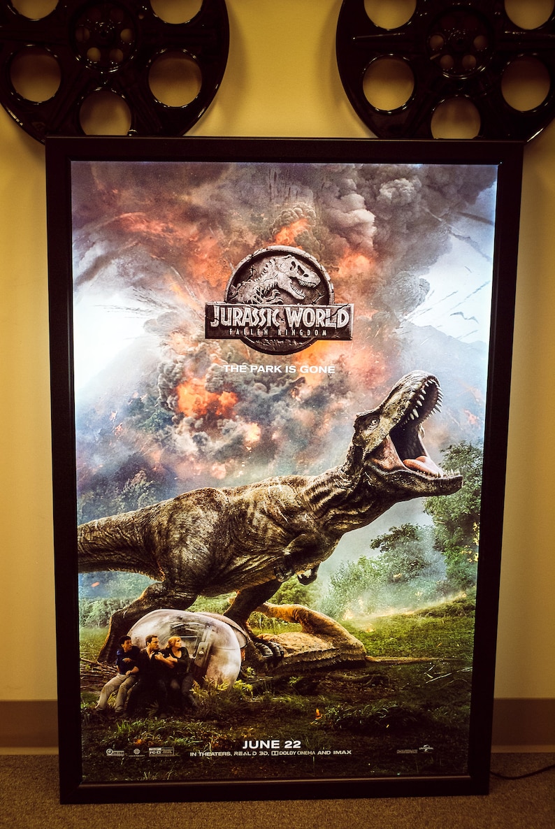 May include: A movie poster for Jurassic World: Fallen Kingdom. The poster features a large, roaring Tyrannosaurus Rex in front of a fiery, cloudy background. The text "Jurassic World: Fallen Kingdom" and "The Park is Gone" are visible on the poster.