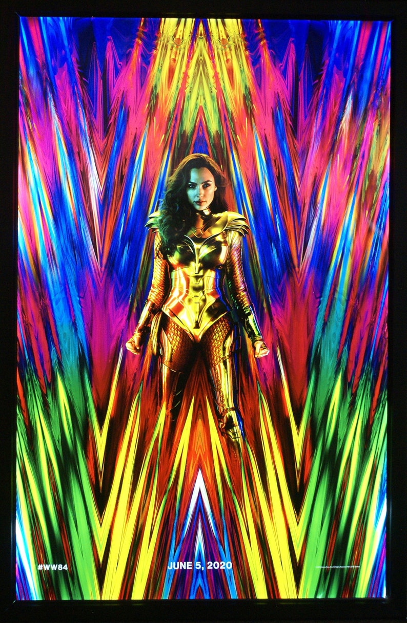 May include: A movie poster for Wonder Woman 1984 featuring Gal Gadot as Wonder Woman in a gold costume standing in front of a colorful, abstract background. The text "JUNE 5, 2020" and "#WW84" are at the bottom of the poster.