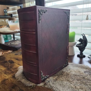 K&ouml;nnte beinhalten: Ein dunkelrotes, ledergebundenes Buch mit verzierten Metallverzierungen und einem Rautenmuster auf dem Einband.