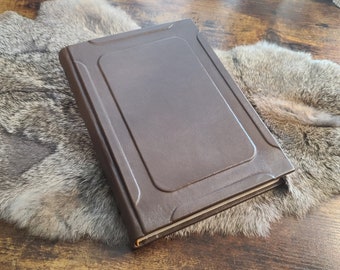 May include: A brown leather-bound journal with a decorative embossed design on the cover. The journal is closed and lying on a faux fur surface.