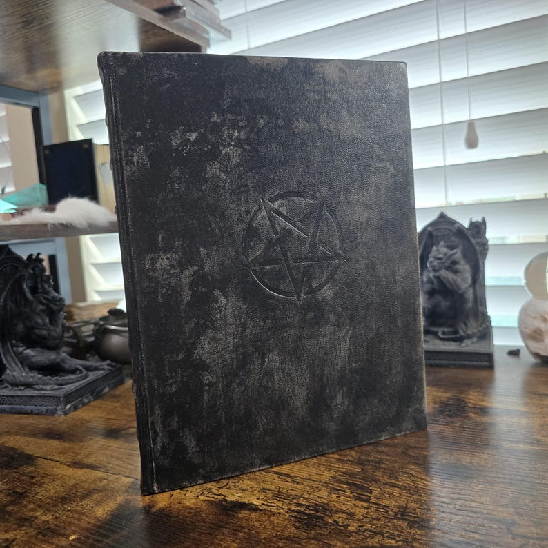 K&ouml;nnte beinhalten: Ein schwarzes, ledergebundenes Tagebuch mit einem gepr&auml;gten Pentagramm auf dem vorderen Umschlag. Der Umschlag hat ein abgenutztes, antikes Aussehen.