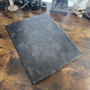 K&ouml;nnte beinhalten: Ein schwarzes, ledergebundenes Tagebuch mit einem gepr&auml;gten Pentagramm auf dem Einband.