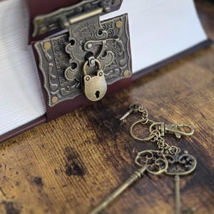 May include: A vintage-style book with a brass lock and key. The book is closed and has a brown leather cover. The key is attached to a keychain with a small metal charm.