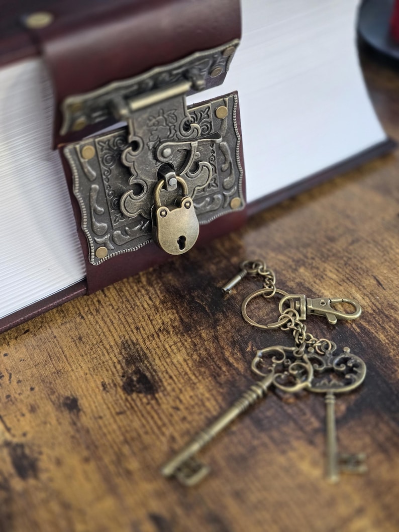 May include: A vintage-style book with a brass lock and key. The book is closed and has a brown leather cover. The key is attached to a keychain with a small metal charm.