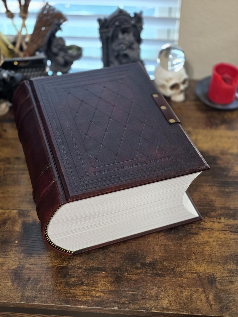 May include: A large, dark brown leather-bound book with a diamond pattern embossed on the cover. The book is closed and lying on a wooden surface.