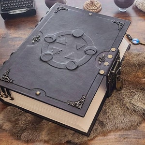 May include: A large, black leather-bound journal with a decorative lock and key. The cover features an embossed design of a pentagram with four moons around it.