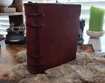 May include: A large, dark red leather-bound book with decorative stitching and a metal clasp. The book is sitting on a faux fur rug.