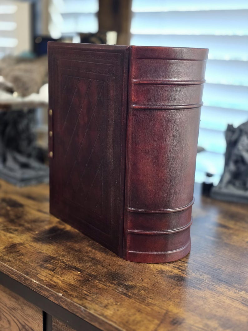 May include: A burgundy leather-bound book with a decorative embossed pattern on the front cover. The book has a spine with three raised bands and is closed.