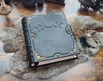 Può includere: Un diario rilegato in pelle nera con un design a fasi lunari in rilievo sulla copertina. Il libro è arricchito da angolari in metallo color ottone, chiusure laterali decorative e due borchie circolari in ottone sui bordi superiore e inferiore.