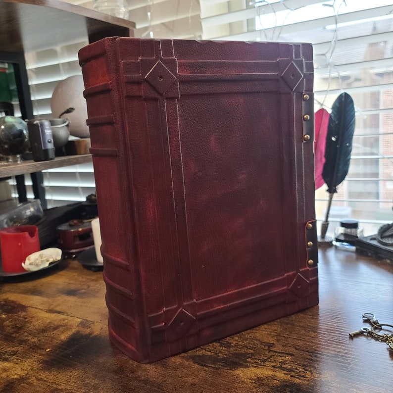 K&ouml;nnte beinhalten: Ein dunkelrotes, ledergebundenes Tagebuch mit dekorativen Metallakzenten und Messingverschl&uuml;ssen. Das Tagebuch hat einen abgenutzten Look und ist geschlossen.