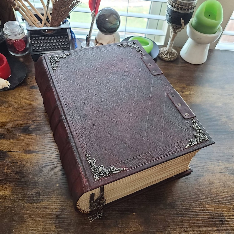 K&ouml;nnte beinhalten: Ein gro&szlig;es, dunkelbraunes, ledergebundenes Buch mit verzierten Metallverzierungen und einem dekorativen Rautenmuster auf dem Einband. Das Buch hat einen abgenutzten, Vintage-Look und ist geschlossen.