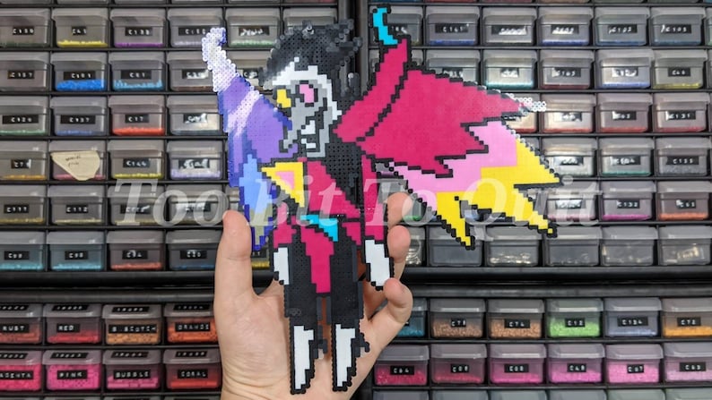 May include: A pixel art figure made of fused plastic beads depicting a character with a white face, black hair, and a large pink and yellow wing. The figure wears a dark suit with a blue tie and has a white arm extended upward.