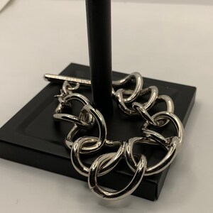 May include: A silver chain bracelet with large, chunky links. The bracelet is displayed on a black stand.