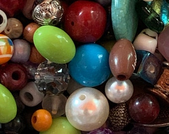 May include: A collection of assorted craft beads in various shapes, sizes, and colors, including round, faceted, and oval styles. The mix features materials such as glass, plastic, and metal, with finishes ranging from opaque and translucent to metallic.