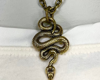 May include: A gold snake pendant necklace with a detailed, textured snake design. The snake is coiled and has a raised head. The necklace is made of a thick, chunky chain.