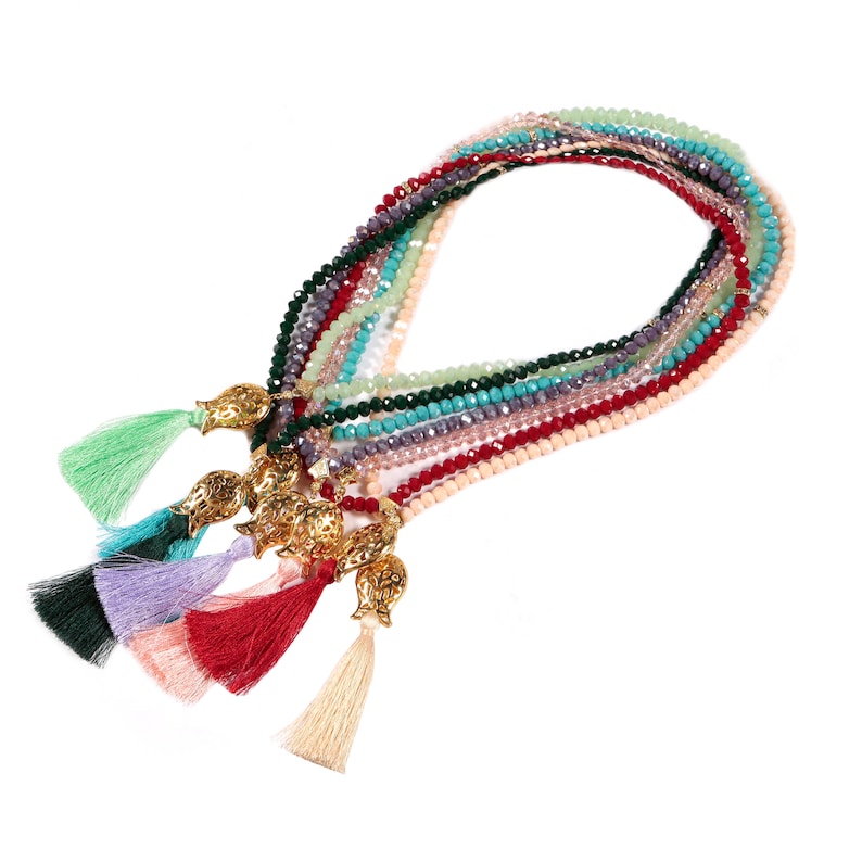 Op de afbeelding: Een meerstrengs ketting met verschillende gekleurde kralen en gouden granaatappelcharms. Elke streng heeft een kwast aan het einde.