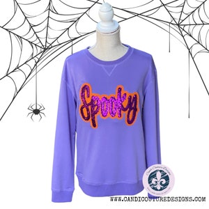 May include: Purple sweatshirt with a sparkly pink and orange "Spooky" design.