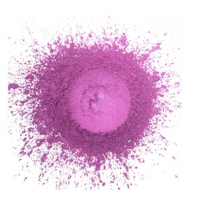 Pu&ograve; includere: Un mucchio circolare di polvere viola vibrante con un centro pi&ugrave; chiaro e iridescente. La polvere &egrave; sparsa sui bordi, creando un effetto schizzo sullo sfondo bianco. La consistenza appare fine e liscia.