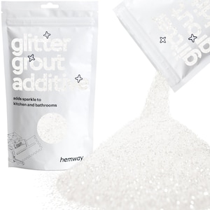 May include: White glitter grout additive in a white pouch. The pouch has the words "glitter grout additive" and "adds sparkle to kitchen and bathrooms" printed on it. Glitter is pouring out of a second pouch.