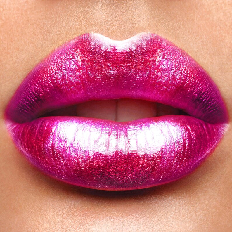 Pu&ograve; includere: Primo piano di labbra piene con un vibrante rossetto fucsia metallizzato. Il rossetto ha una finitura lucida e riflettente, che evidenzia i contorni naturali delle labbra. Il labbro superiore ha un arco di Cupido definito e il labbro inferiore &egrave; pieno e liscio.