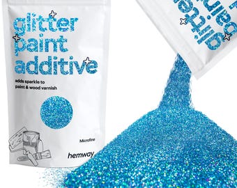 May include: A white bag of blue glitter paint additive with the text "glitter paint additive" and "adds sparkle to paint & wood varnish". Glitter is pouring out of a second bag, forming a large pile.