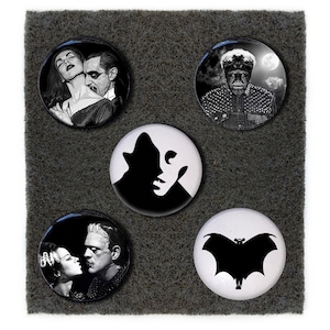 May include: Set of five black and white round buttons featuring classic horror movie characters. The buttons feature a vampire couple, a werewolf, Frankenstein's monster, and a bat.