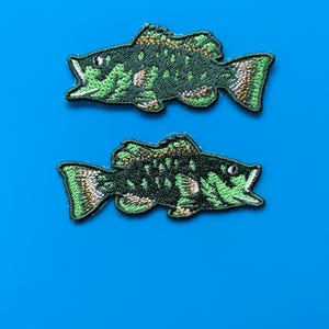 Peut inclure: Deux patchs de poissons brodés de couleur verte et or sur un fond bleu.