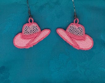 May include: A pair of pink embroidered cowboy hat earrings. The earrings feature a detailed design with a mesh crown and a curved brim. The earrings are suspended from silver-colored fish hook ear wires.