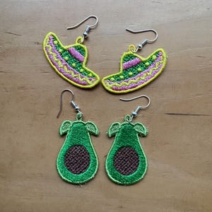 May include: Embroidered earrings featuring two pairs of designs: sombrero hats with yellow, green, and pink details, and avocado halves with green and brown colours. The earrings have silver-coloured hooks.