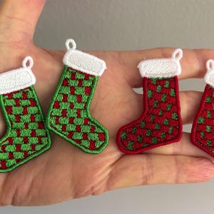 May include: Four miniature Christmas stocking patches. Two are green with red accents, and two are red with green accents. Each stocking has a white cuff and a small loop for hanging.