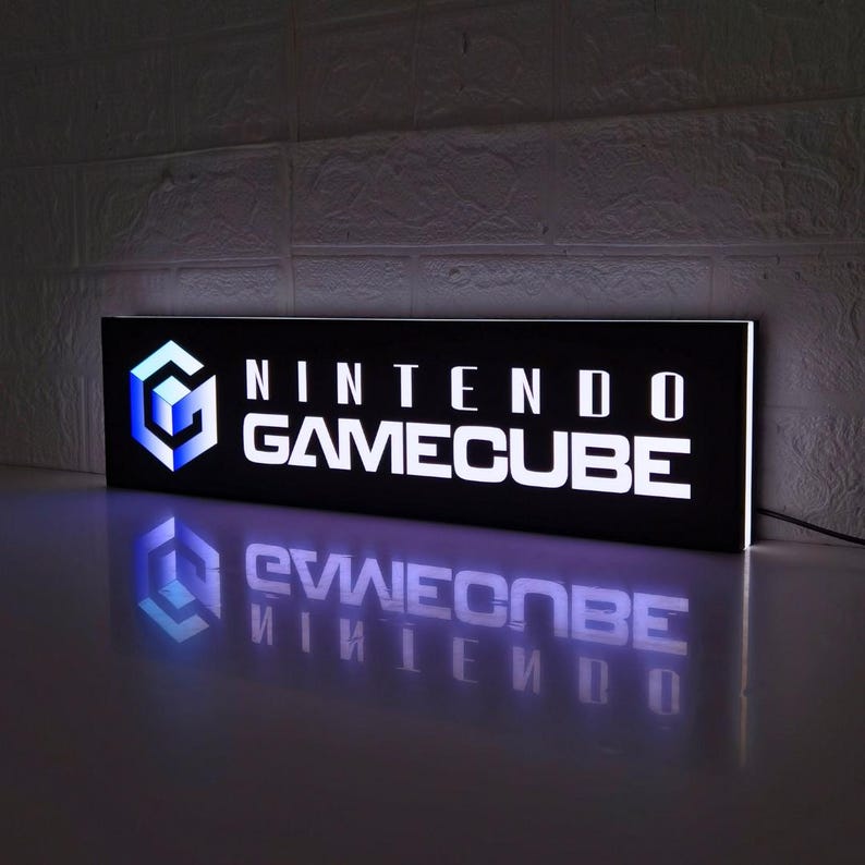 May include: A black and white illuminated sign with the text "NINTENDO GAMECUBE" in white letters. The sign is reflecting on a dark surface.