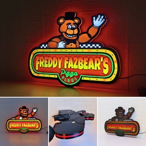 May include: A wall-mounted LED sign featuring a cartoon brown bear character waving, positioned above a yellow and green oval frame with the text "FREDDY FAZBEAR'S PIZZA PLACE" in red and yellow lettering, with a black power cord attached.