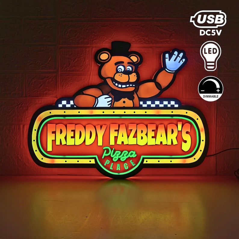 May include: A light-up LED sign featuring a cartoon brown bear character wearing a black top hat and bowtie, waving a hand. The sign displays the text 'FREDDY FAZBEAR'S PIZZA PLACE' in yellow and green lettering, with USB DC5V and dimmable icons.
