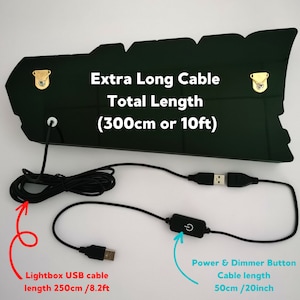May include: A dark green rectangular lightbox with two gold-colored metal mounting brackets on the back. The text reads: Extra Long Cable Total Length (300cm or 10ft). It includes a black USB cable measuring 250cm/8.2ft and a 50cm/20inch power and dimmer button cable.