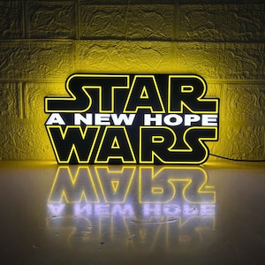 Könnte beinhalten: Ein gelbes und schwarzes Neon-Schild mit dem Text "STAR WARS A NEW HOPE" in weißen Buchstaben. Das Schild spiegelt sich auf einer Oberfläche.