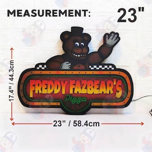 May include: A Freddy Fazbear's Pizza sign featuring a brown bear character waving, with orange and yellow text on a dark background. The sign measures 23 inches in width and 17.4 inches in height, with a black power cord extending to the right side.