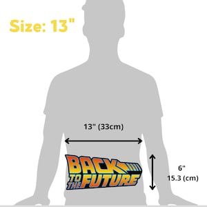 Op de afbeelding: Een Back to the Future-logo, 33 cm breed en 15,3 cm hoog, wordt getoond. Het logo toont de woorden "BACK TO THE FUTURE" in oranje, geel en blauw, met een futuristisch lettertype. De grootte is 13 inch.