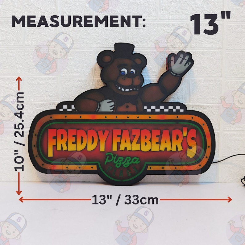 May include: A Freddy Fazbear's Pizza Place sign featuring a brown bear character waving. The sign measures 13 inches wide by 10 inches tall. The text reads "FREDDY FAZBEAR'S Pizza PLACE" in yellow and green lettering against a dark background.