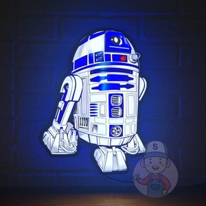 Könnte beinhalten: Ein blaues und weißes Nachtlicht mit der Figur des Roboters R2-D2 vor einem Hintergrund aus Ziegeln.