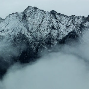 May include: A snowy mountain range with a thick layer of fog covering the lower slopes.