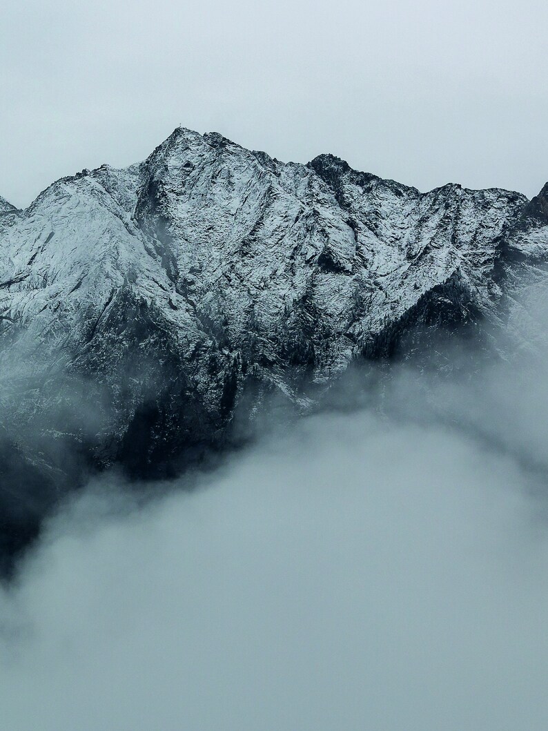 May include: A snowy mountain range with a thick layer of fog covering the lower slopes.